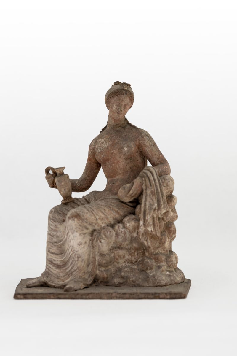 Tanagra représentant une femme assise sur un rocher