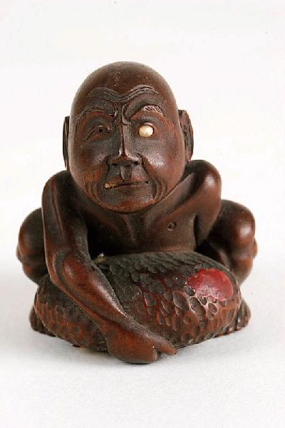 Netsuke en forme d'un homme, borgne, accroupi, tentant de soulever une pierre