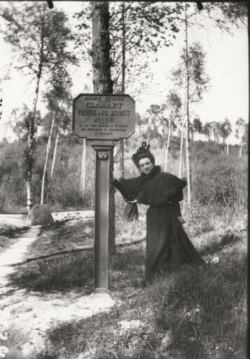 Portrait d'archéologue. Mme Fourdrignier (?) devant le poteau indicateur du menhir 'Pierre aux moines' de la ville de Clamart
