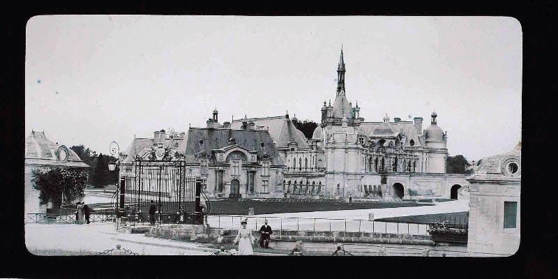 Le château de Chantilly vue de la Grille d'Honneur avec un jardinier et l'arrosage automatique des pelouses, vers 1898-1900 ; Photographie panoramique positive sur plaque de verre (vue prise avec la stéréopanoramique Mackenstein)