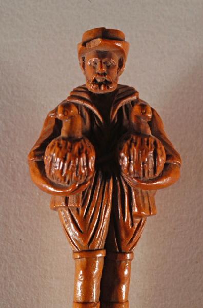 Bâtonnet de bois sculpté en forme de colonne en bois noir surmonté d'une statuette de bois représentant un paysan tenant un canard sous chaque bras