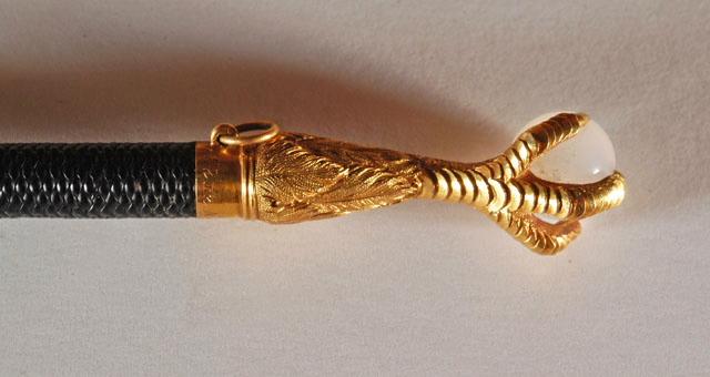 Cravache en cuir noir avec à l'extrémité une serre d'aigle en or tenant une pierre semi-précieuse blanche