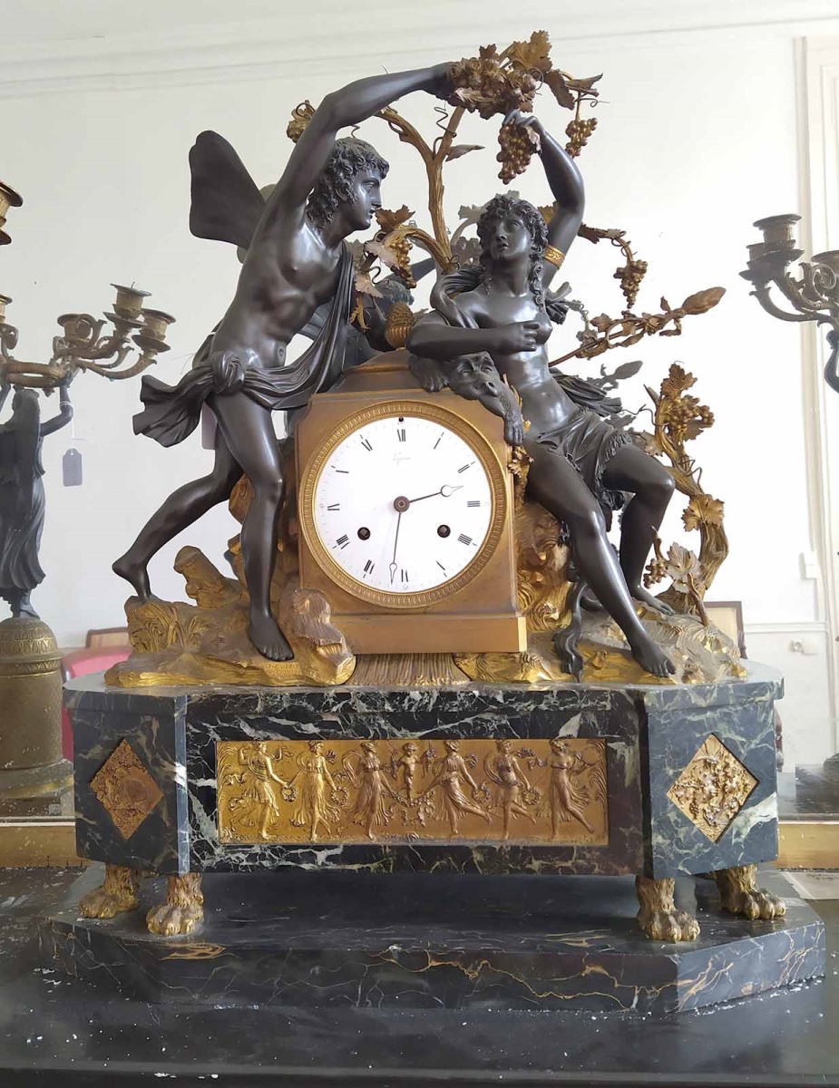 Pendule avec deux personnages en bronze patiné, un jeune homme ailé qui tend une grappe de raisin à une jeune femme
