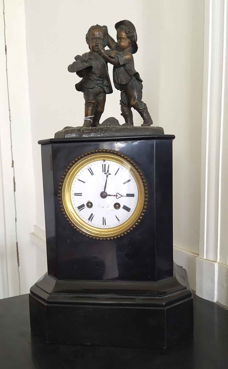 Pendule en marbre noir surmontée de deux enfants en bronze qui se battent pour deux chiots