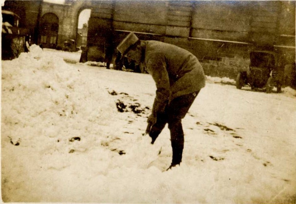 Un militaire dégageant la neige aux Grandes Ecuries de Chantilly, avec à l’arrière-plan deux automobiles du G.Q.G. entre 1914 et 1916 ; 11 photographies anonymes encartées dans des montages détachés d’un petit album : Le domaine de Chantilly pendant la guerre de 14-18, photos du Grand Quartier Général en février-mars 1916