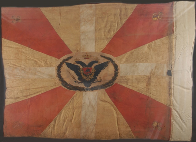 Drapeau en tissu crème broché à motif floral avec croix de Malte rose et et croix latine blanche, avec un aigle noir à deux têtes couronné au centre et 4 fleurs de lys d’or aux angles