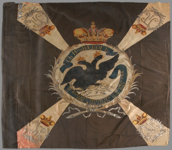 Drapeau noir avec croix de Malte rose, avec un aigle noir à deux têtes couronné au centre et 4 fleurs de lys d’or aux angles et une inscription en russe