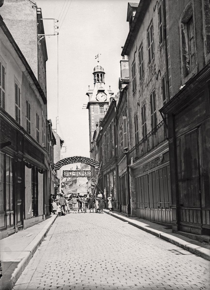 Nuits-Saint-Georges - “SOYEZ LES BIENVENUS”. Enfilade de la Grande rue avec le beffroi au fond à droite (titre usuel)