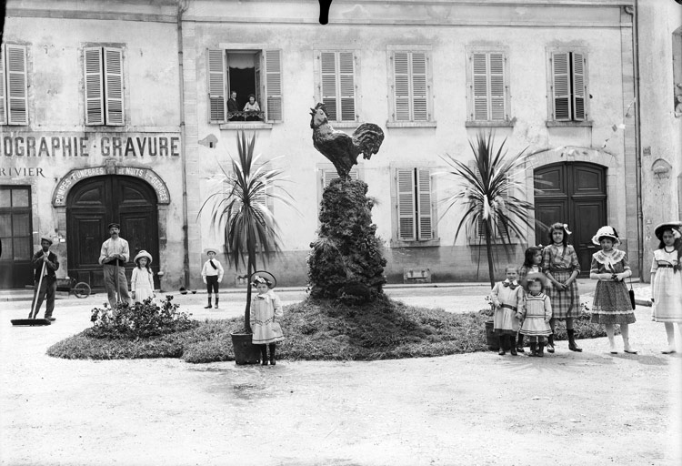 Homme au travail et enfants devant les pompes funèbres. Sur la place, coq sur un piédestal et palmiers en pot : Place Monge (titre usuel)