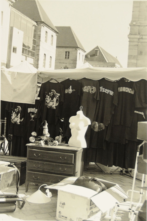 Besançon 2012, place de la Révolution, jour de marché Au premier plan, objets divers mis en vente par un brocanteur qui se détachent sur un fond noir constitué de kakémonos portant une inscription ou l'effigie de Bob Marley