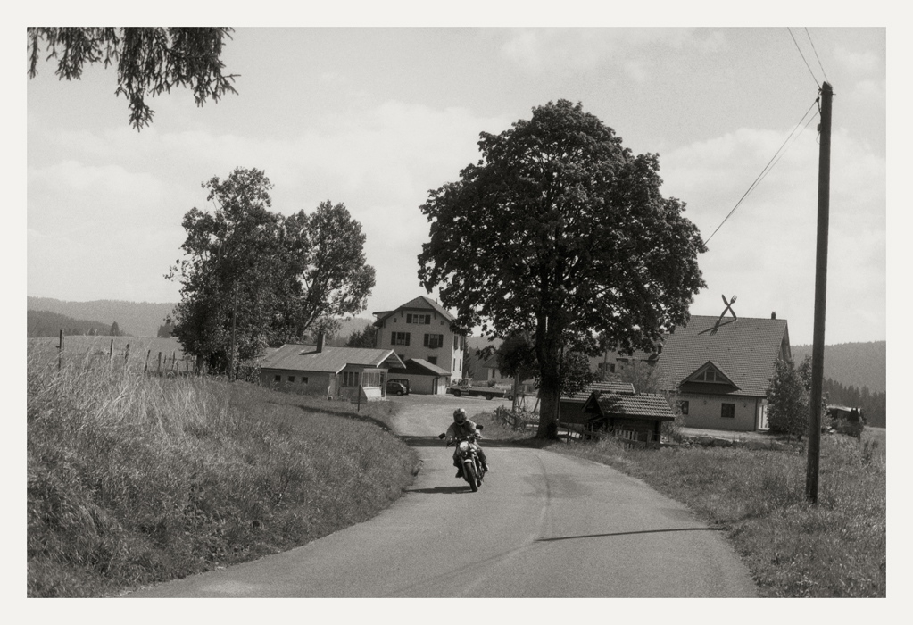 Photographié en 2008, motocycliste sur une route ; à l'arrière-plan sur la droite, un restaurant caractérisé par un couvert géant sur le toit
