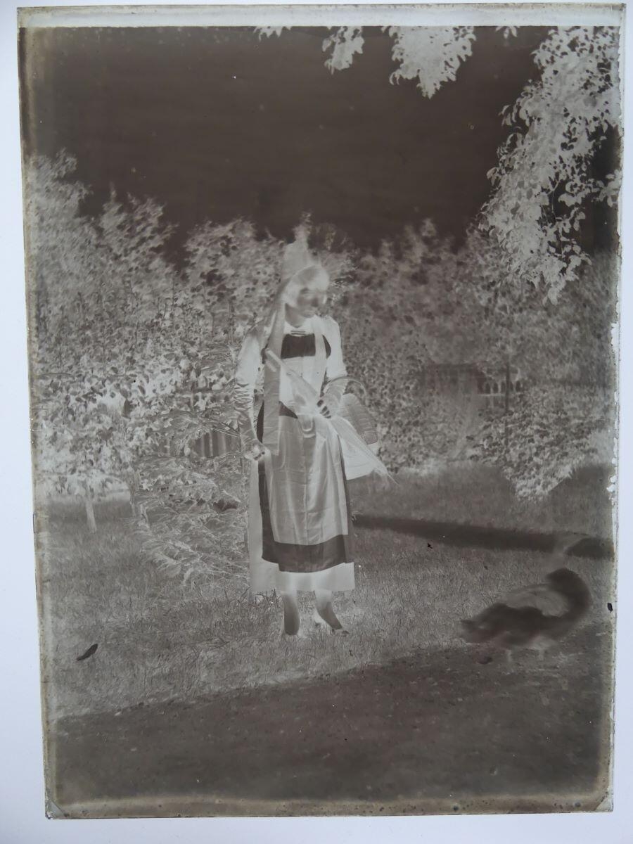 Jeune femme en costume régional, tenant un parapluie fermé, dans un jardin