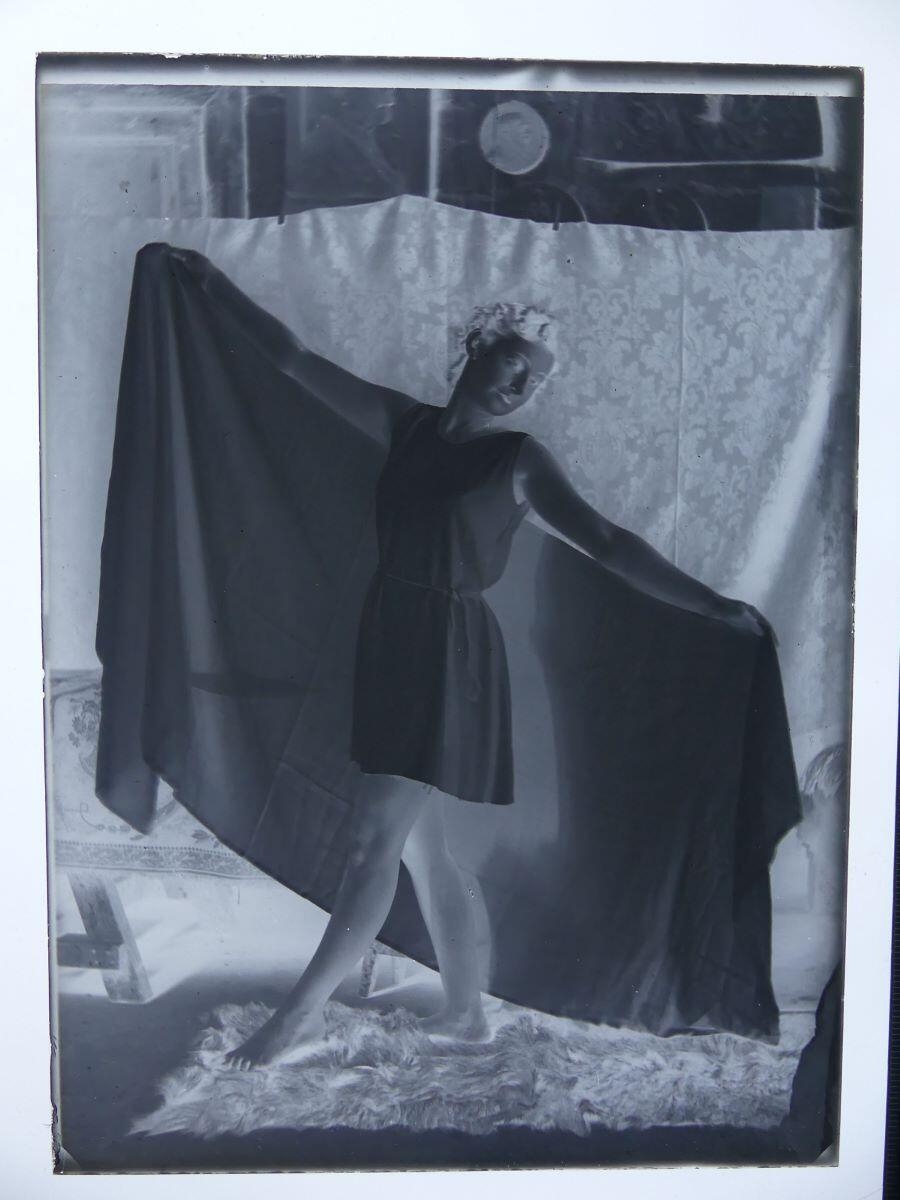 Modèle féminin posant dans l'atelier, debout, les bras ouverts et tenant un voile derrière elle