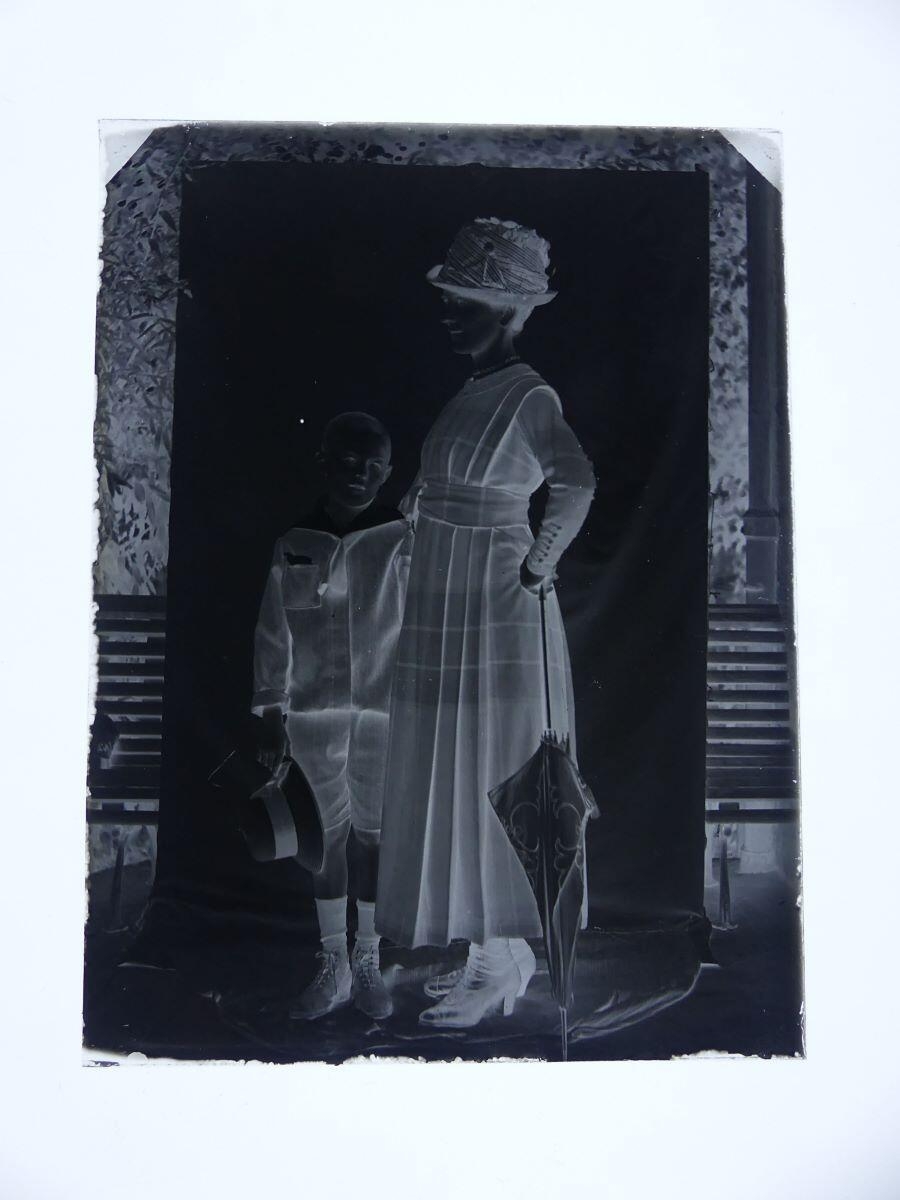 Louise Hertig, de profil, appuyée sur une ombrelle et son fils James, enfant, posant en extérieur, devant un rideau