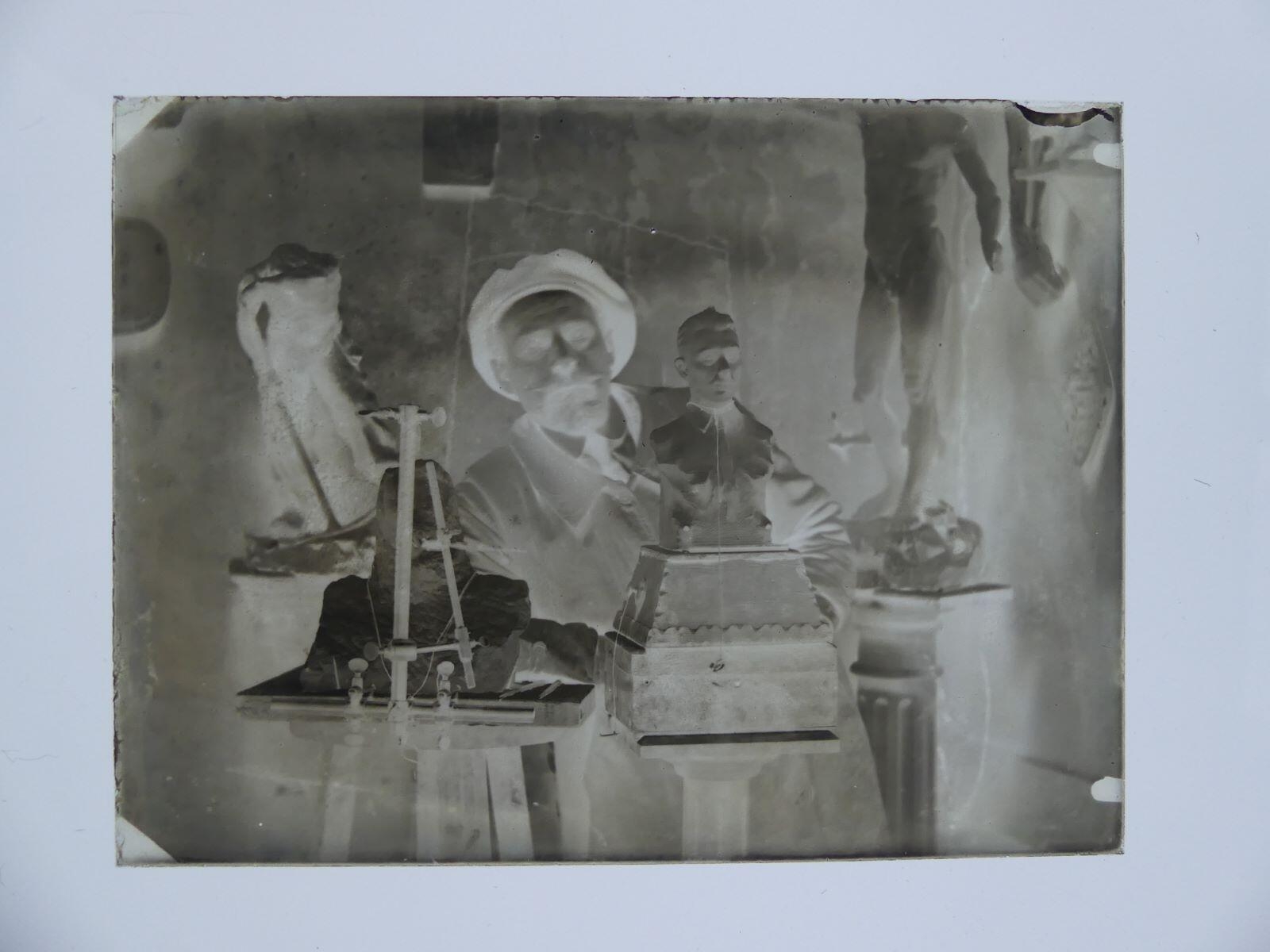 Portrait de Louis Hertig dans son atelier posant derrière des oeuvres en cours de création, notamment le portrait en plâtre de George