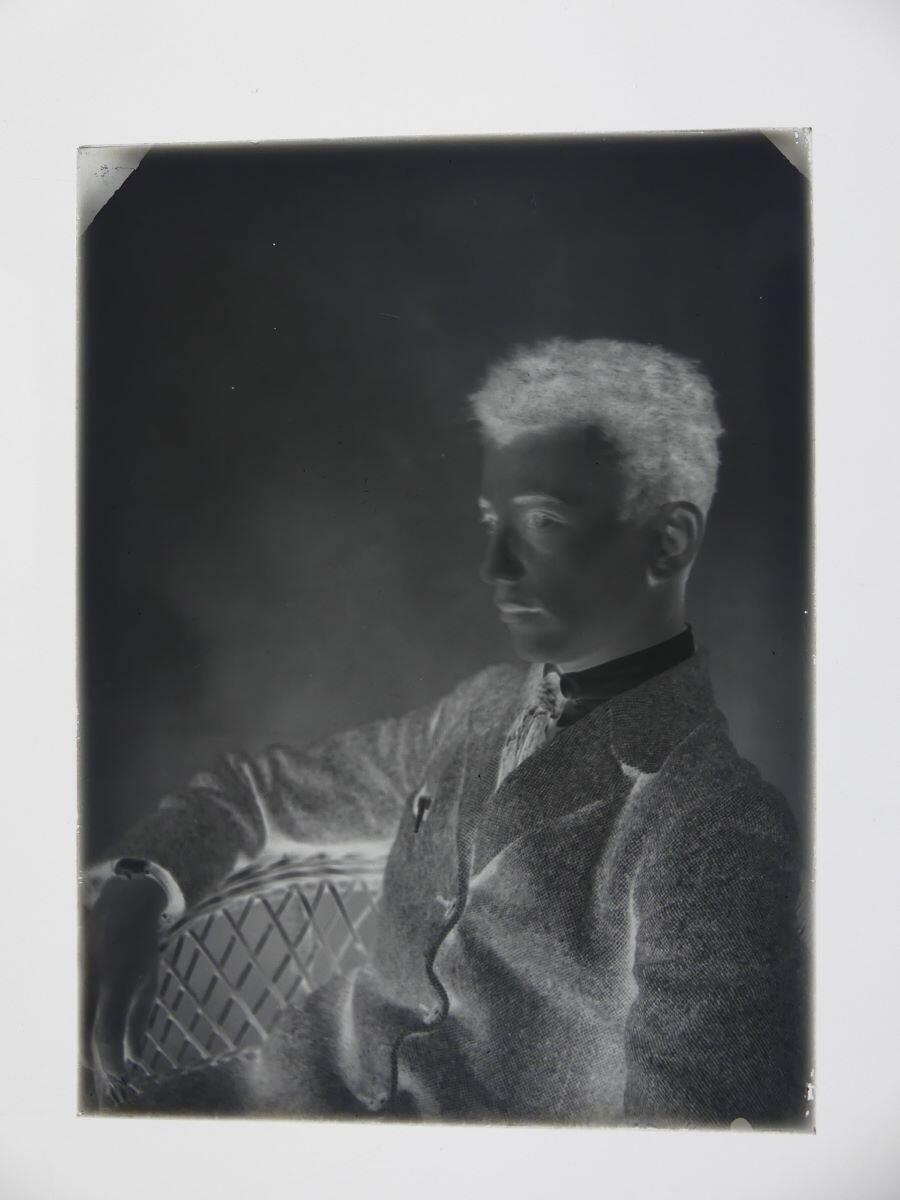 Portrait de jeune homme assis de 3/4 droit dans un fauteuil en rotin