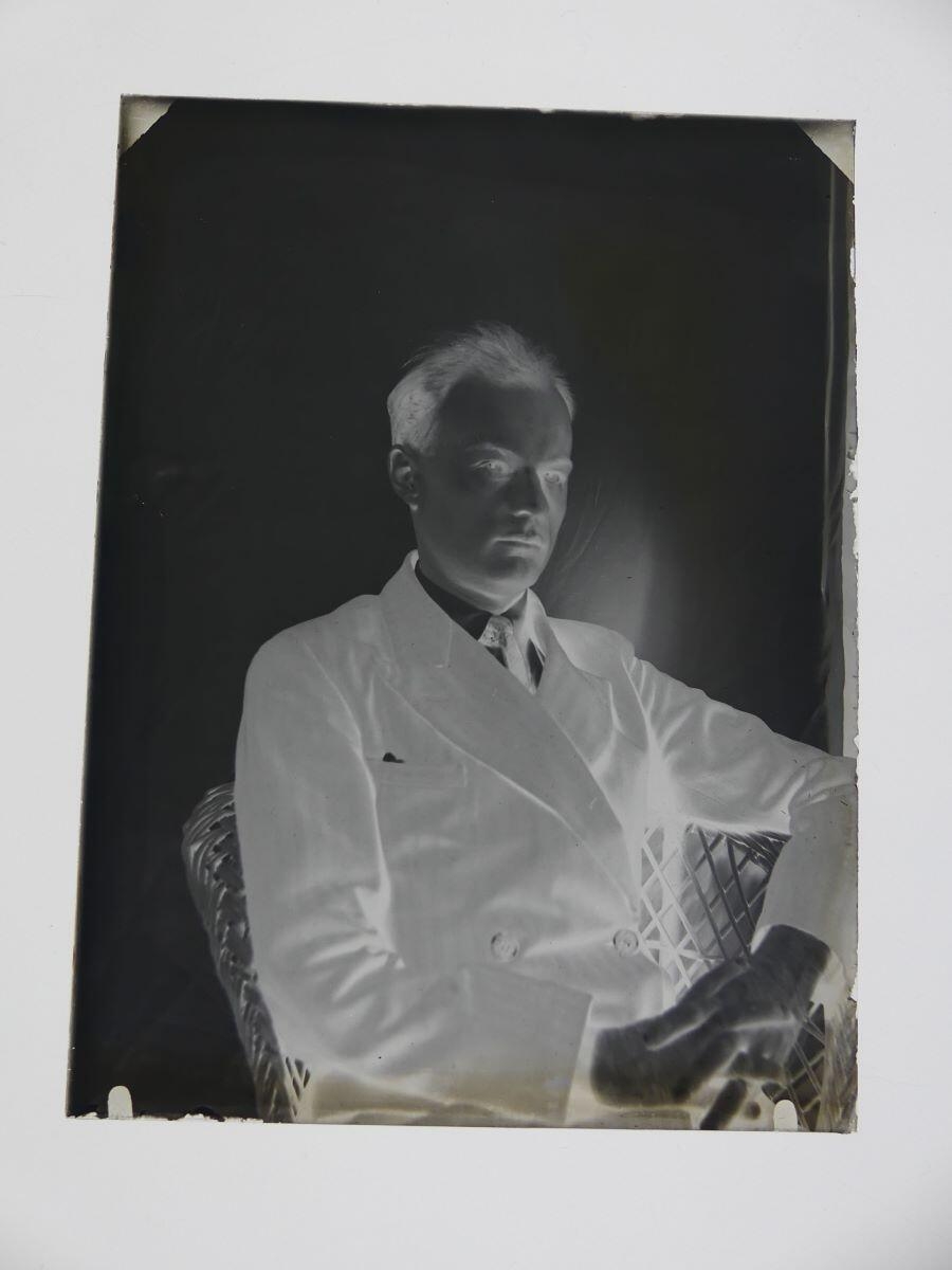 Portrait de James Hertig adulte posant assis dans un fauteuil en osier