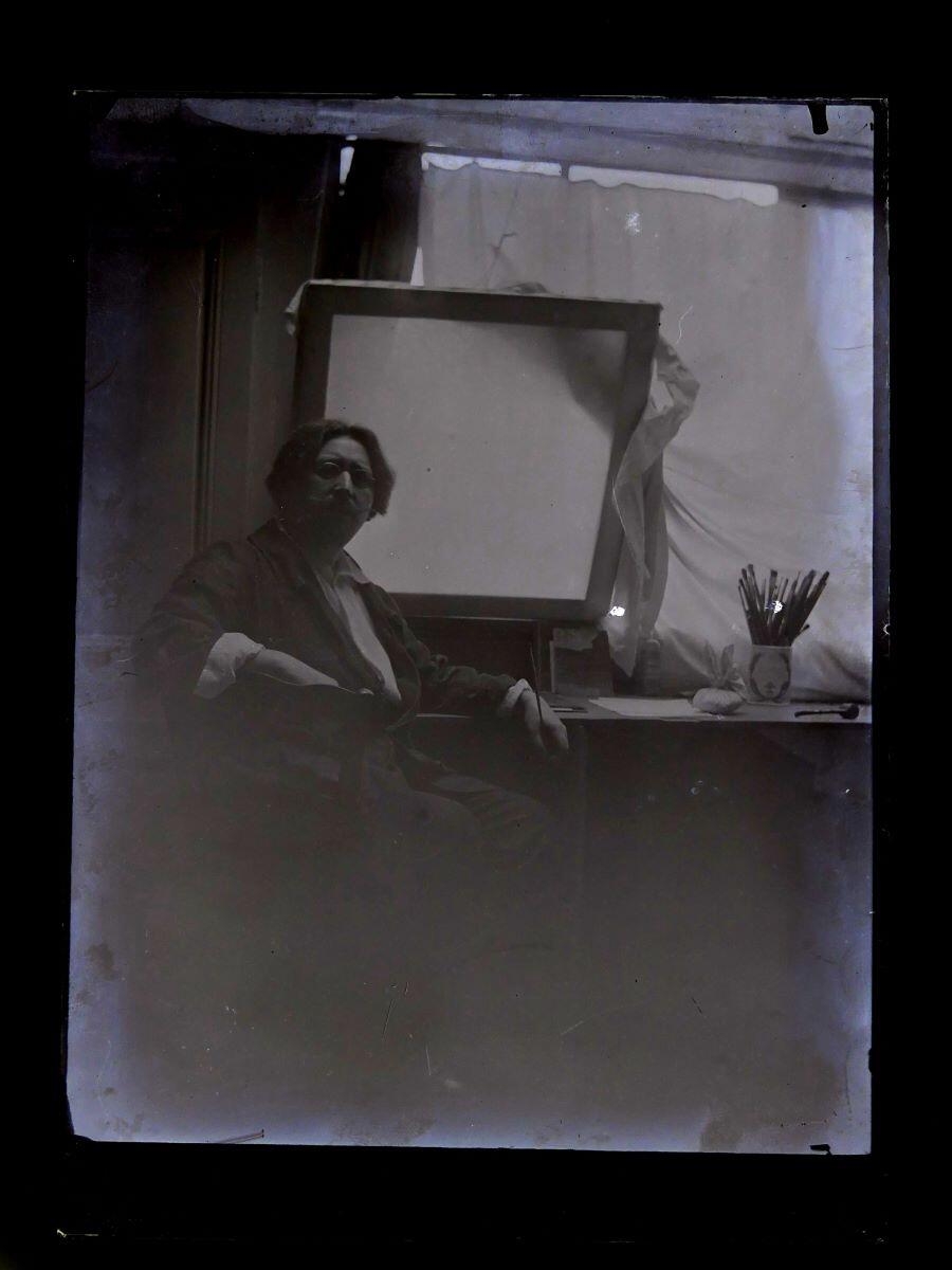 Portrait du peintre Léon Tirode dans son atelier assis devant une table de travail, assis sur la gauche