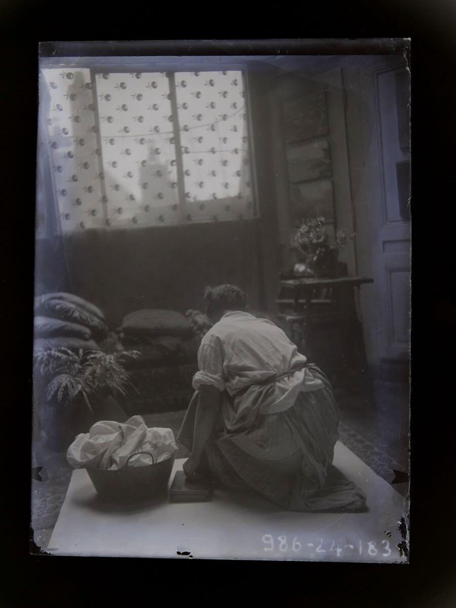 Femme accroupie, vue de dos, à côté d'une corbeille de linge