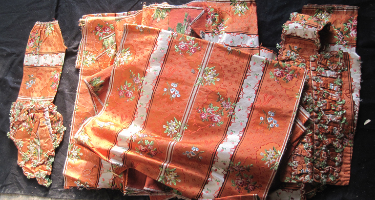 Deux manches et quinze morceaux de brocart rouge à rayures torsadées de blanc (dont un avec des boutons)