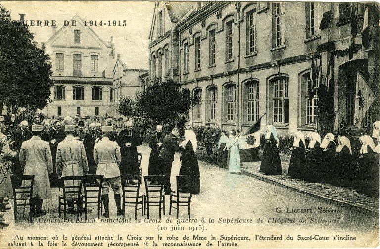 Guerre 1914-1915 - Le Général Jullien remettant la Croix de guerre à la Supérieure de l'Hôpital de Soissons (10 juin 1915). Au moment où le général attache la Croix sur la robe de Madame la Supérieure, l'étendard du Sacré-Coeur s'incline saluant à la fois le dévouement récompensé et la reconnaissance de l'armée