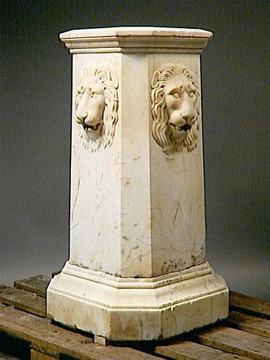 FONTAINE EN FORME DE GAINE CARREE ET CHANFREINEE ORNEE SUR SES QUATRE FACES D'UNE TETE DE LION, AVEC GOULOTS EN PLOMB