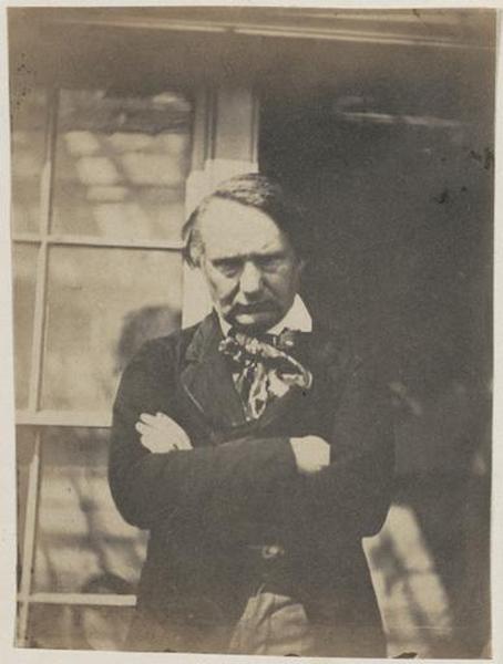 Victor Hugo debout, les bras croisés, devant la porte de la serre de Marine Terrace